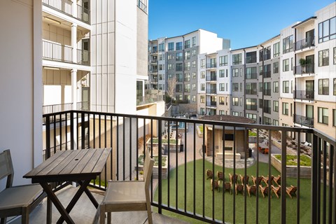 A balcony with a table and chairs overlooks a courtyard with a fence and a small garden.