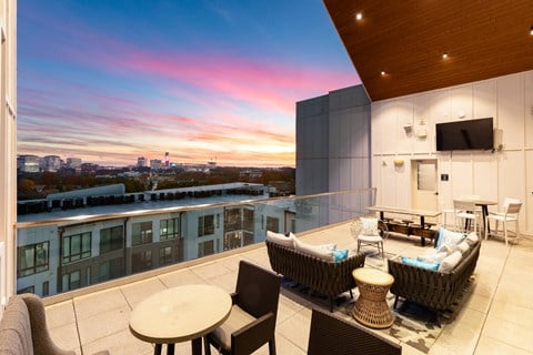 A balcony with a table and chairs overlooking a cityscape at sunset.