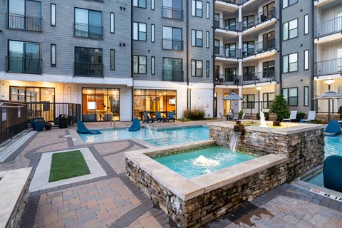 A large outdoor swimming pool with a waterfall and a hot tub in front of a multi-story apartment building.