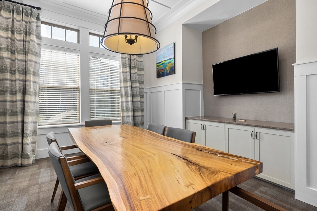 A wooden dining table with chairs and a television mounted on the wall.