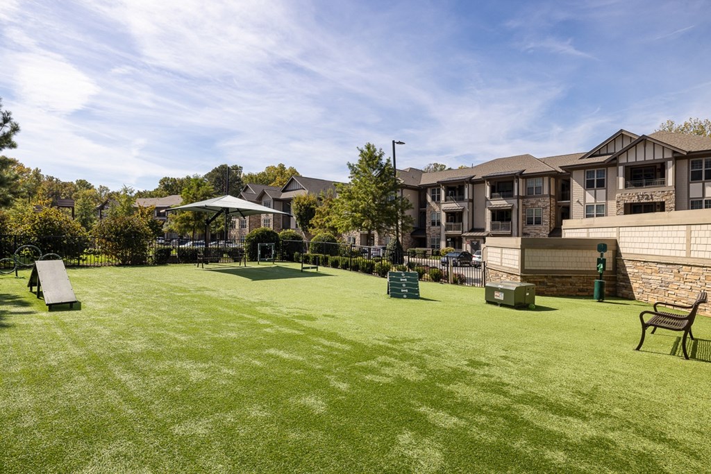 A grassy field with a bench and a playground in the background.