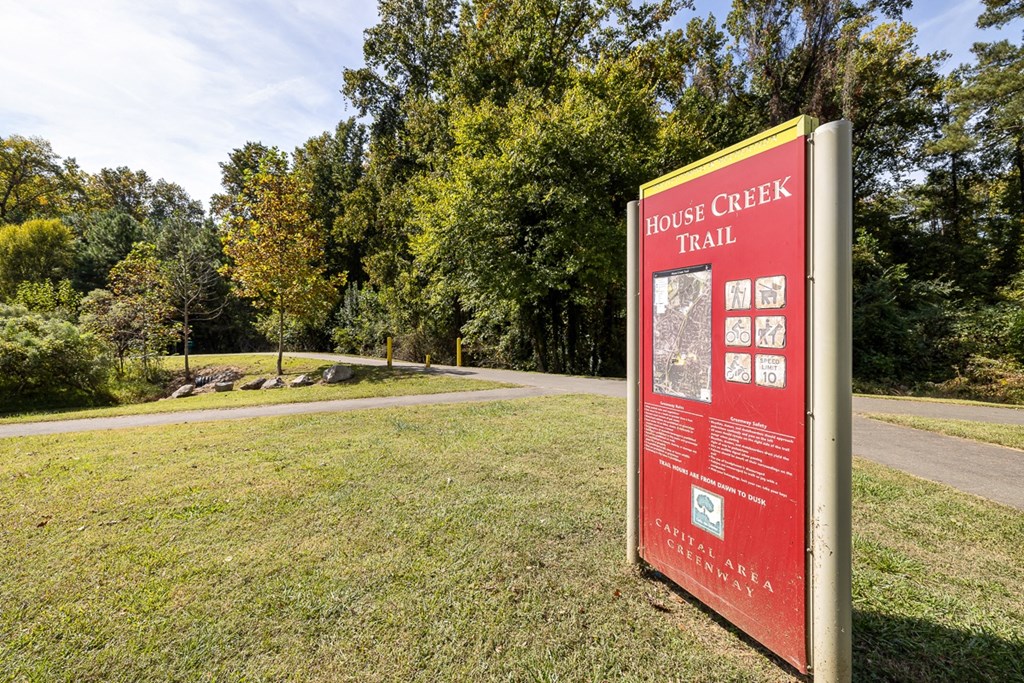 A sign for the House Creek Trail stands in a grassy area with trees in the background.