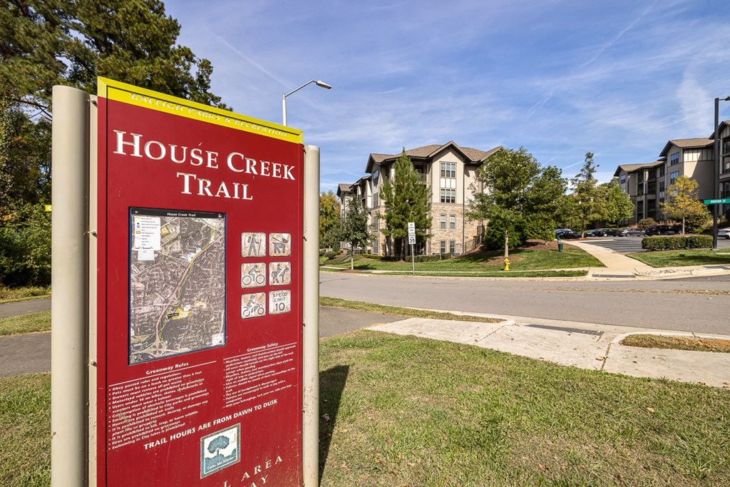 A sign for the House Creek Trail stands in the foreground of a residential street.