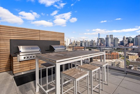 A rooftop patio with a grill and stools overlooking a city skyline.