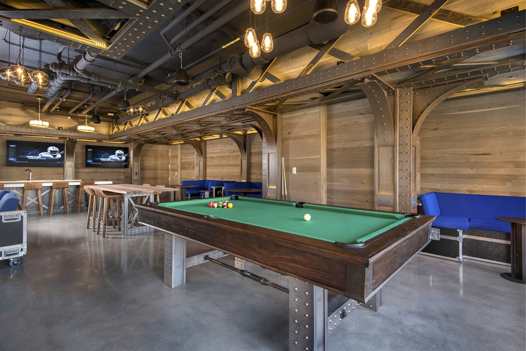 A pool table in a room with a high ceiling and exposed pipes.