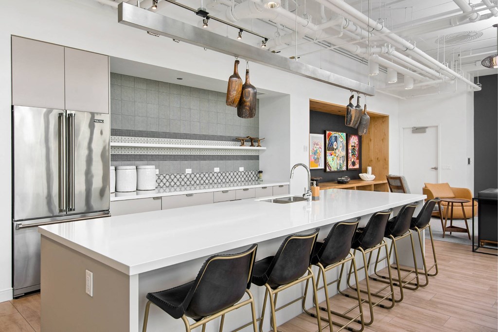 A kitchen with a long white counter and black chairs.