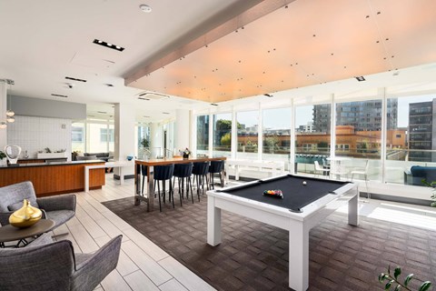 A billiard table is in the middle of a room with a kitchen area and a balcony.