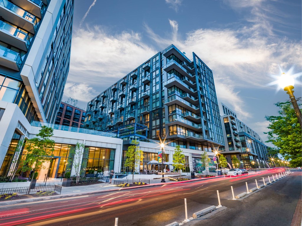 A modern building with a blue facade is illuminated by street lights at dusk.