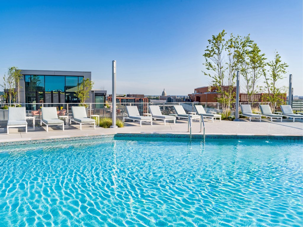 A swimming pool with sun loungers and a modern building in the background.