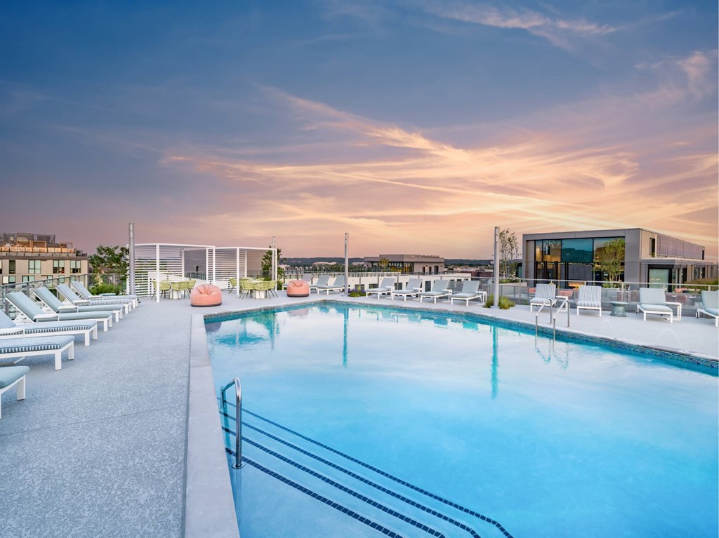 A large outdoor swimming pool with lounge chairs and a building in the background.