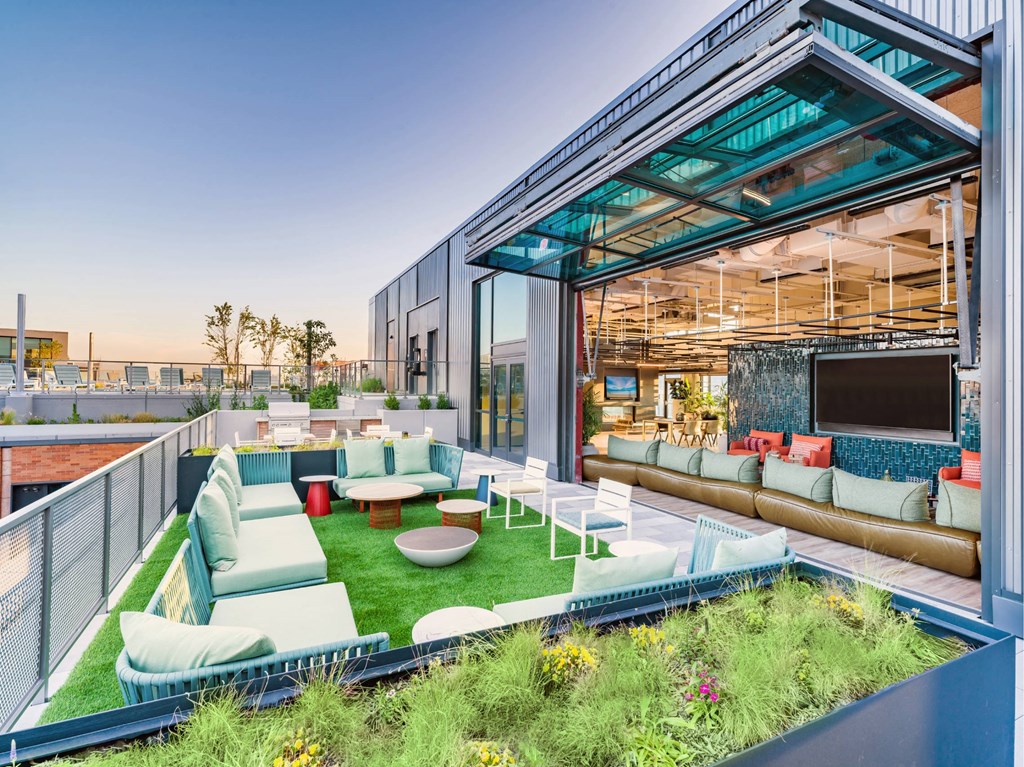 A modern outdoor seating area with a glass ceiling and a green lawn.