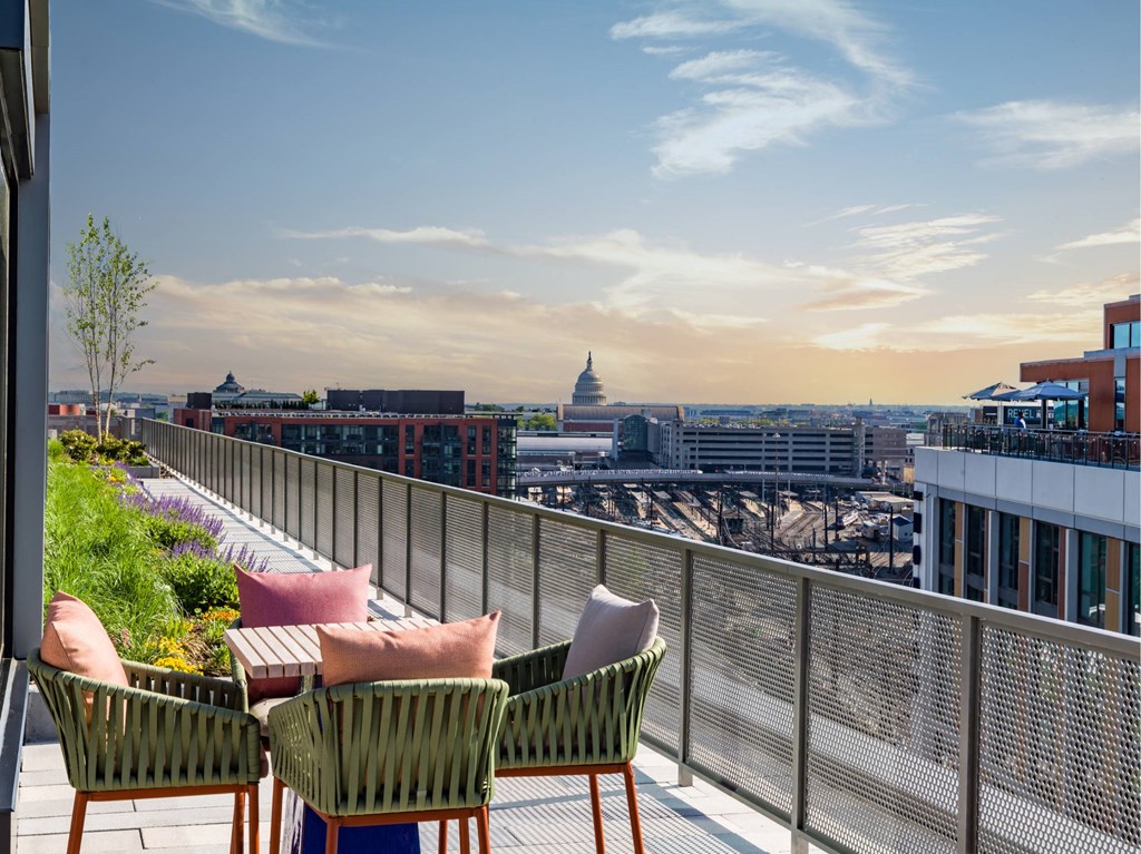 Two chairs and a table on a balcony overlooking a cityscape.