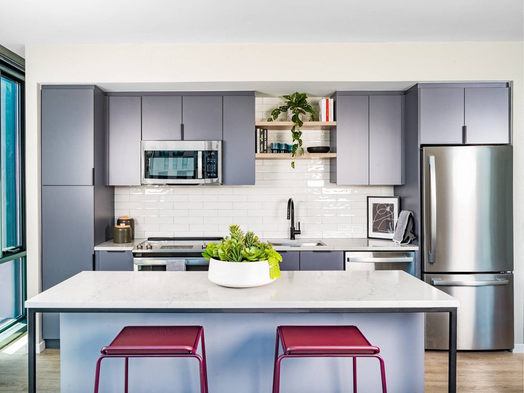 A modern kitchen with a white island and red stools.