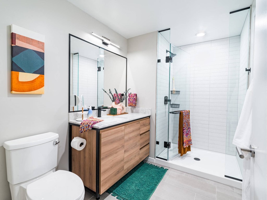 A bathroom with a white toilet, a wooden vanity, and a glass shower.