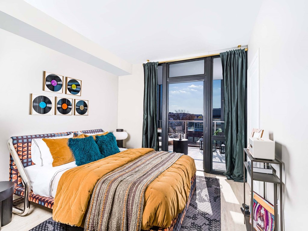 A bedroom with a bed, a nightstand, and a window with a view of the city.