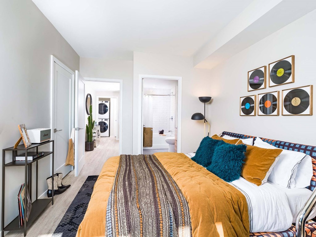 A bedroom with a bed, a nightstand, and a wall with framed records on it.