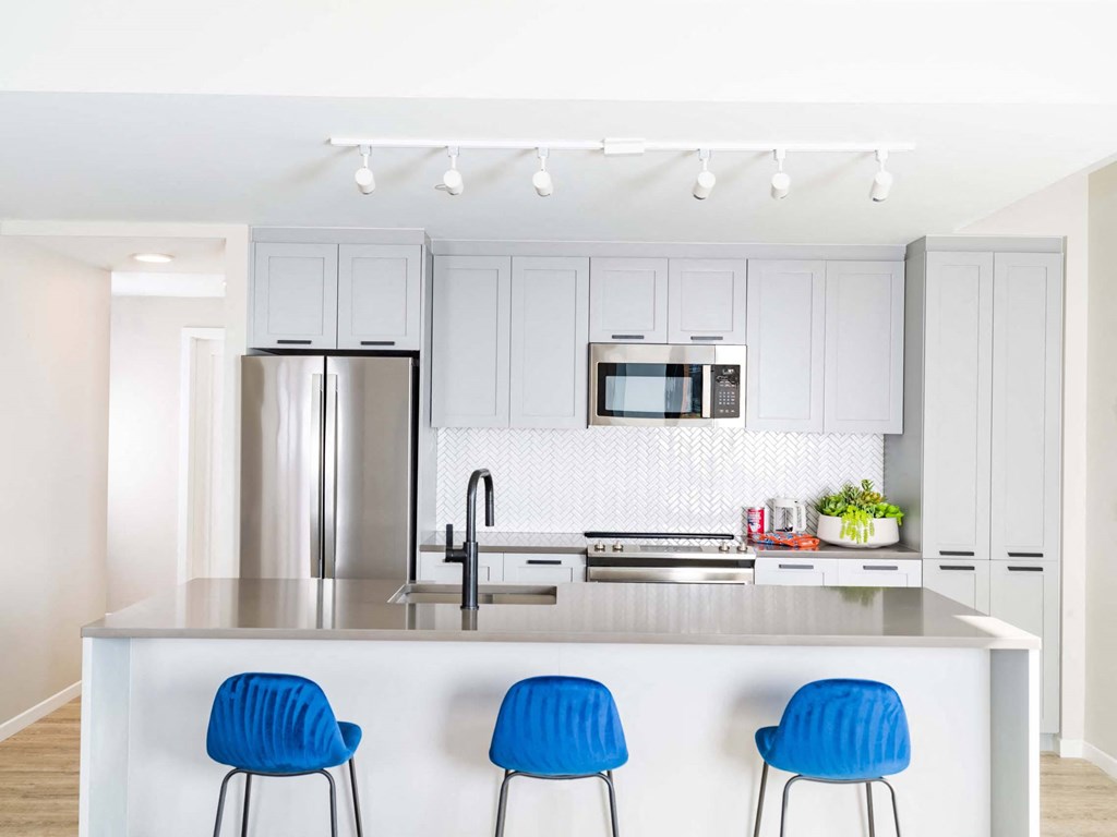 A modern kitchen with a white island and blue chairs.