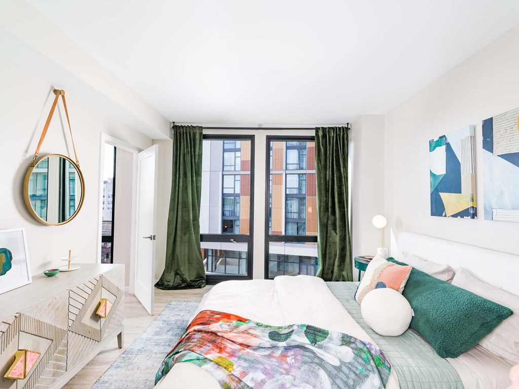 A bedroom with a large bed and a window with green curtains.