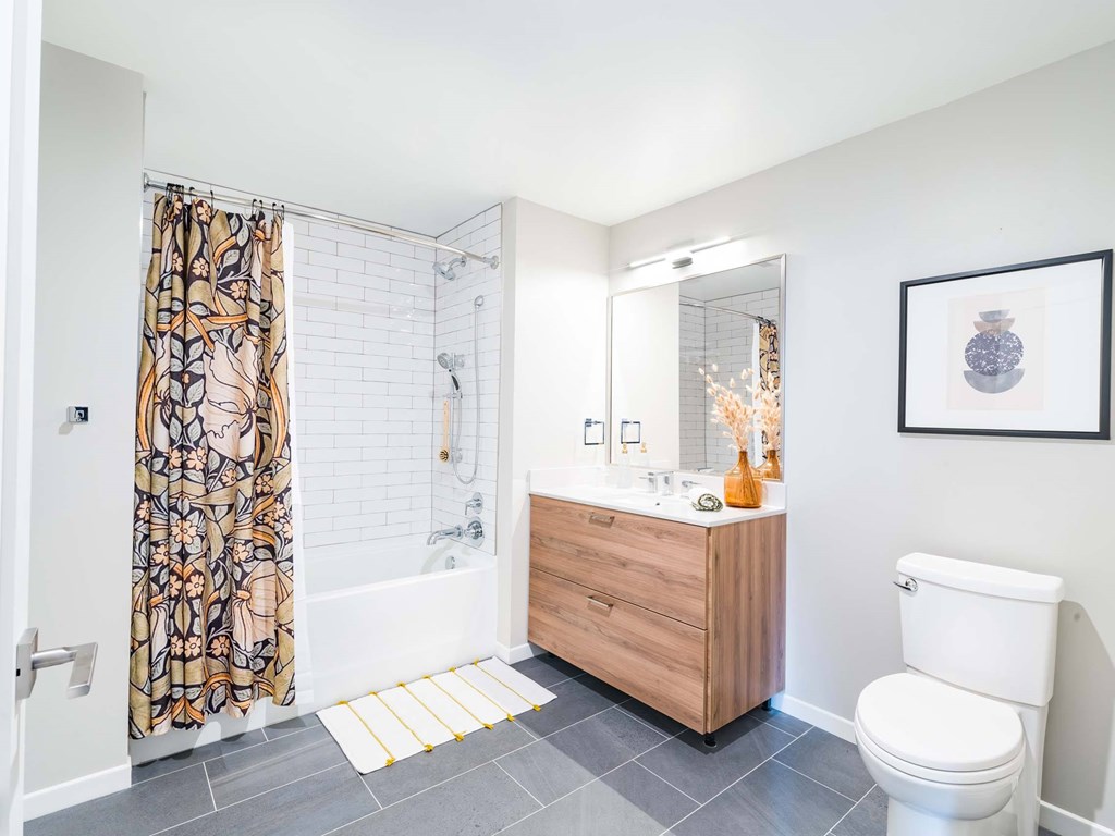A bathroom with a white toilet, a wooden vanity, and a shower with a patterned curtain.