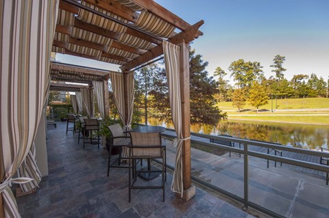 A wooden pergola with curtains and chairs overlooking a pond.