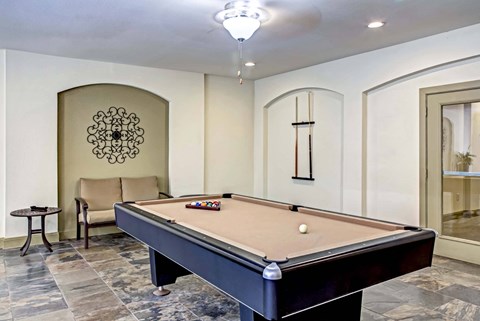 A pool table in a room with a chair and a decorative wall hanging.