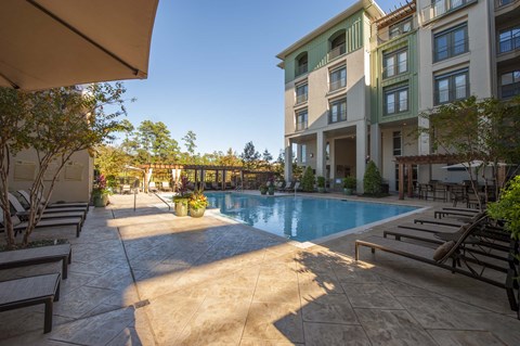 A pool area with sun loungers and a building in the background.