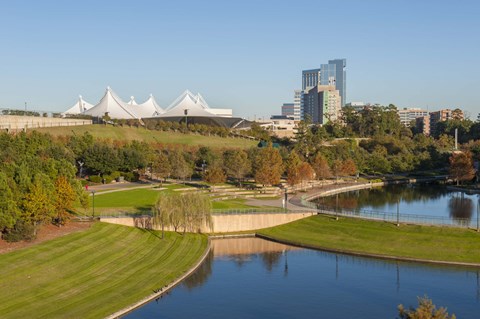 A large white building with a curved roof is situated in the middle of a green field with a lake in front of it.