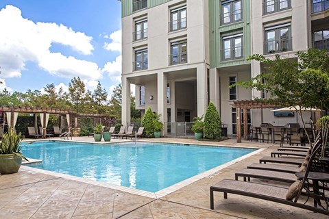 A large swimming pool is surrounded by lounge chairs and potted plants.