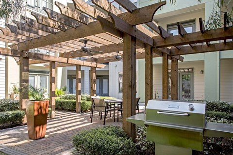 A BBQ grill is in the middle of a patio with a pergola over it.