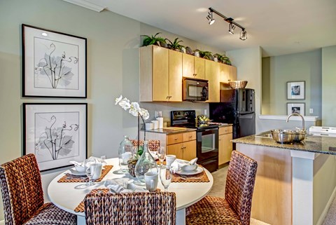 A kitchen with a table set for two with chairs around it.