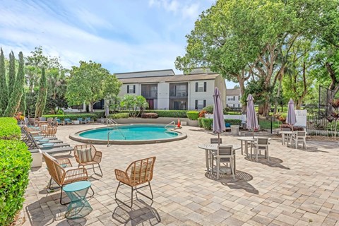 A pool surrounded by chairs and umbrellas with a building in the background.