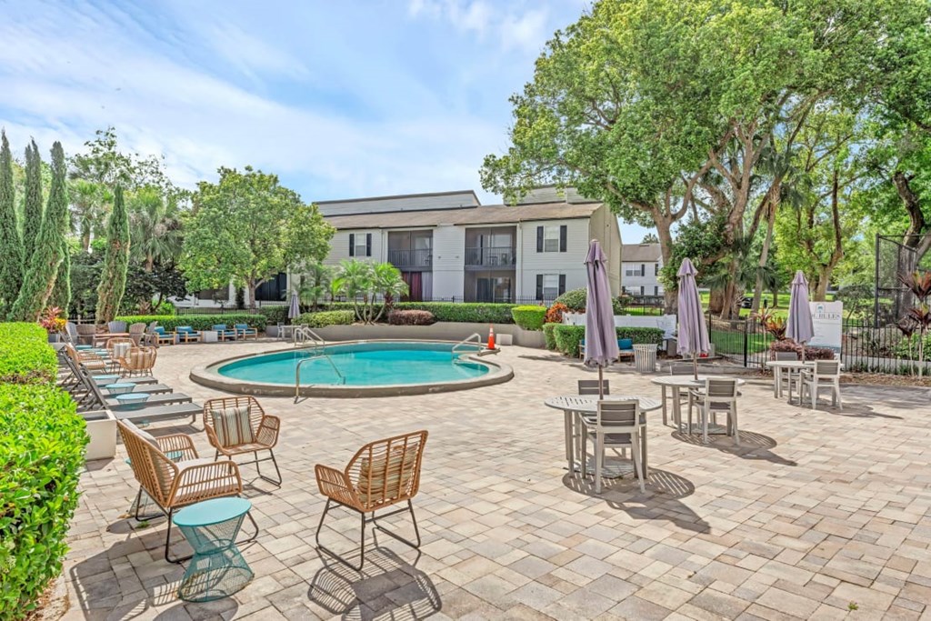A pool surrounded by chairs and umbrellas with a building in the background.