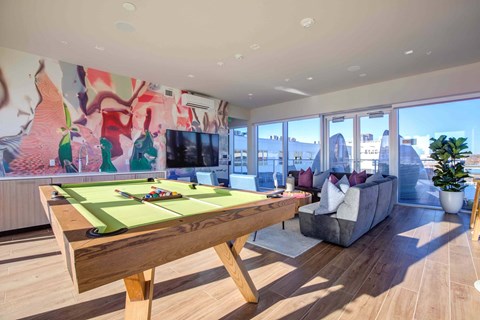 A pool table in a room with a couch and a plant.