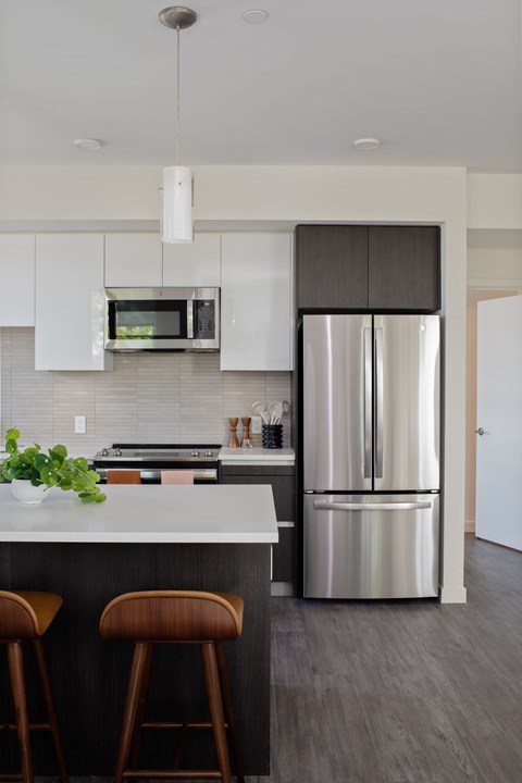 A modern kitchen with a stainless steel refrigerator and bar stools.