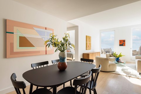A dining room with a table and chairs and a painting on the wall.