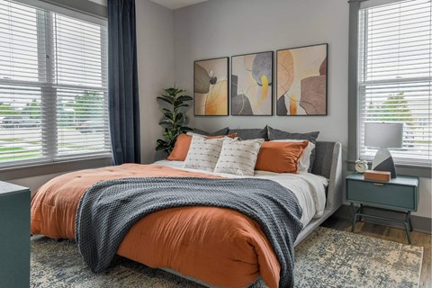 A bedroom with a bed covered in an orange comforter and a grey throw.