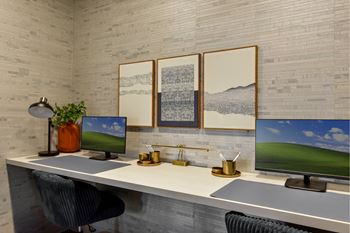 A modern office with a white desk, two monitors, and a chair.