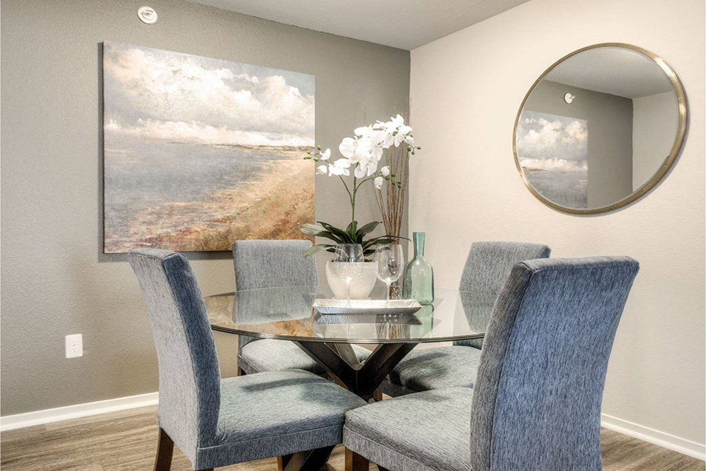A dining room with a table set for four and a painting of a beach scene on the wall.