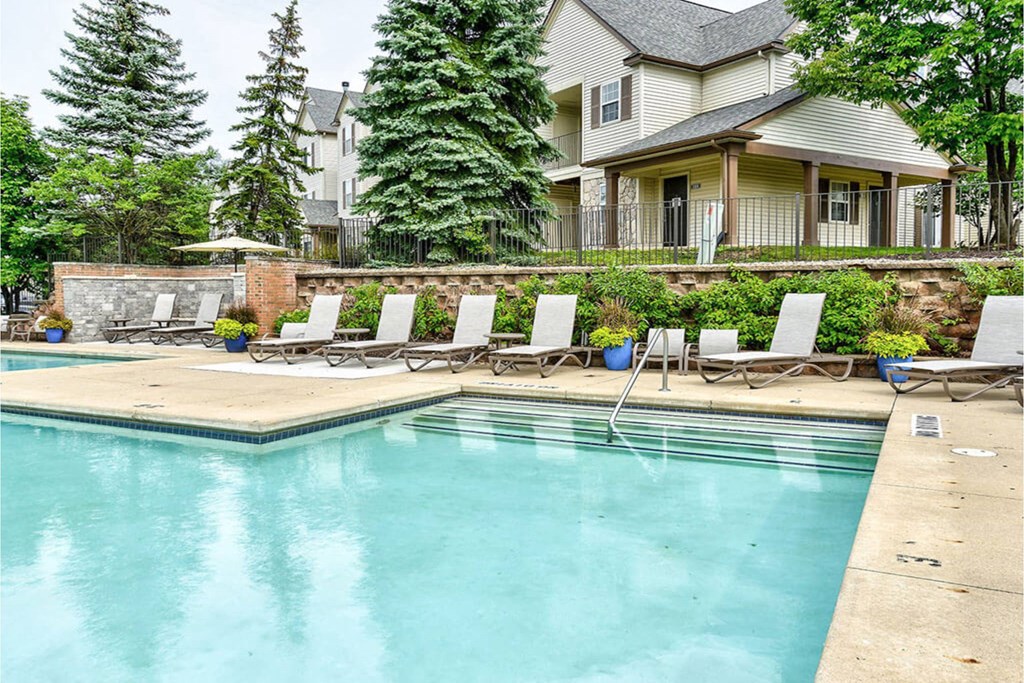 A pool with a few chairs and a house in the background.