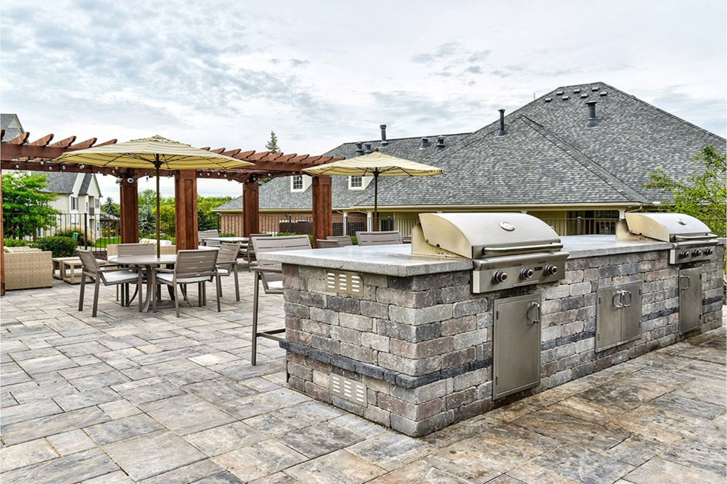 A patio with a stone barbecue and chairs under a pergola.
