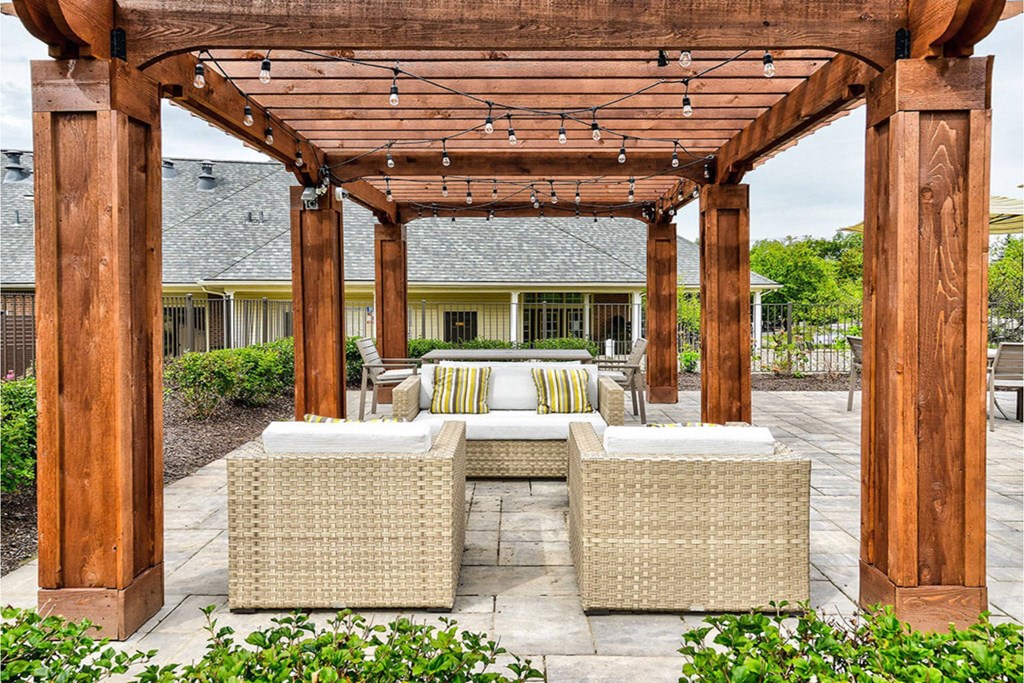 A patio with a wooden pergola and wicker furniture.