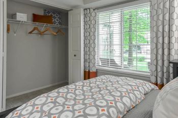A bedroom with a bed, a window with curtains, and a closet with clothes hanging.