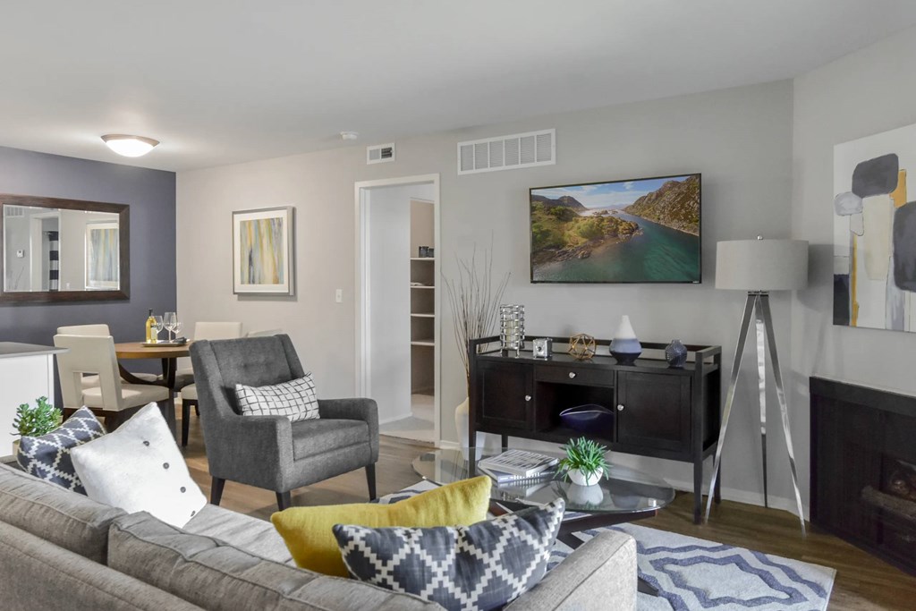 A living room with a grey couch, a grey armchair, a yellow and grey pillow, a grey and white blanket, a grey and white throw, a grey and white pillow, a grey and white throw, a grey