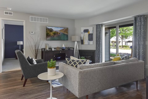 A living room with a grey couch, a grey chair, a white table, and a painting on the wall.