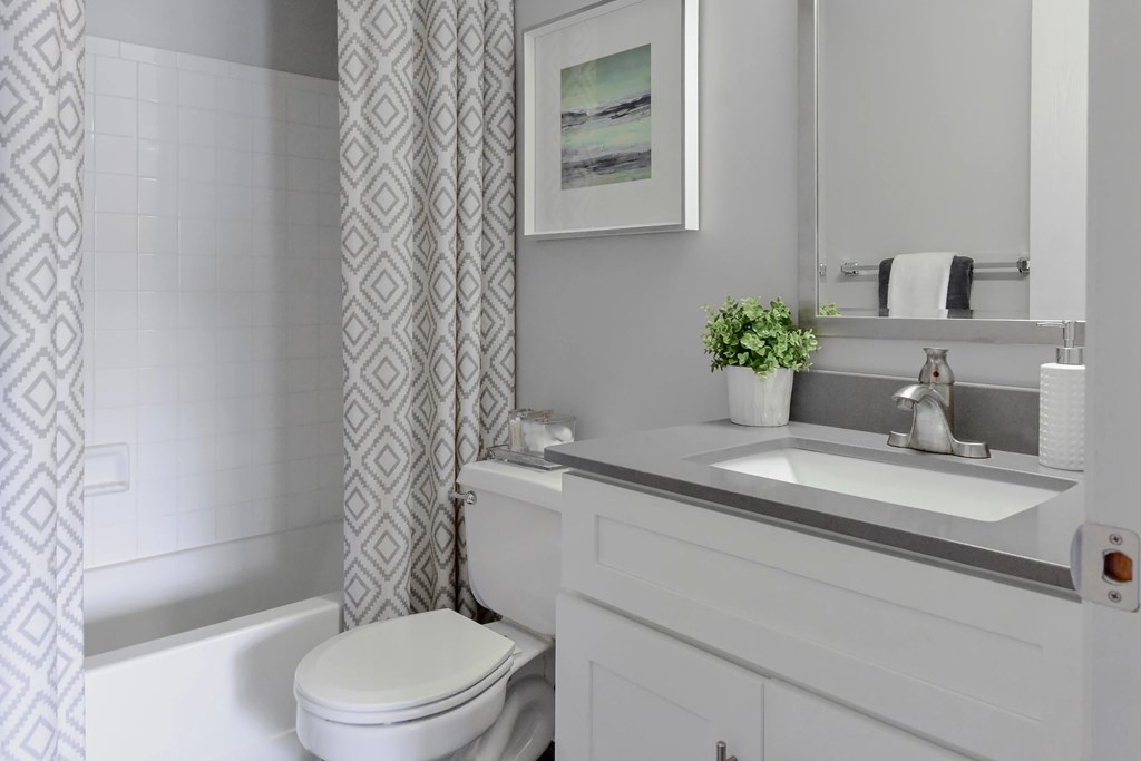 A white bathroom with a toilet, sink, and a framed picture on the wall.