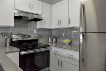 A modern kitchen with a stove, refrigerator, and cabinets.