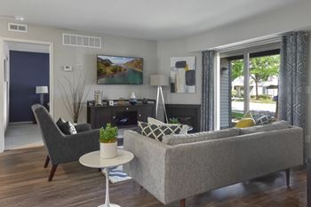 A living room with a grey couch, a grey chair, a white table, a plant, and a painting on the wall.