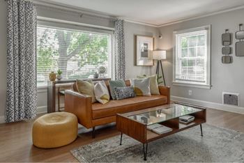 A living room with a brown couch, a glass coffee table, and a yellow pouf.