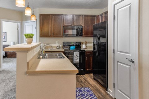 A kitchen with a black refrigerator and brown cabinets.