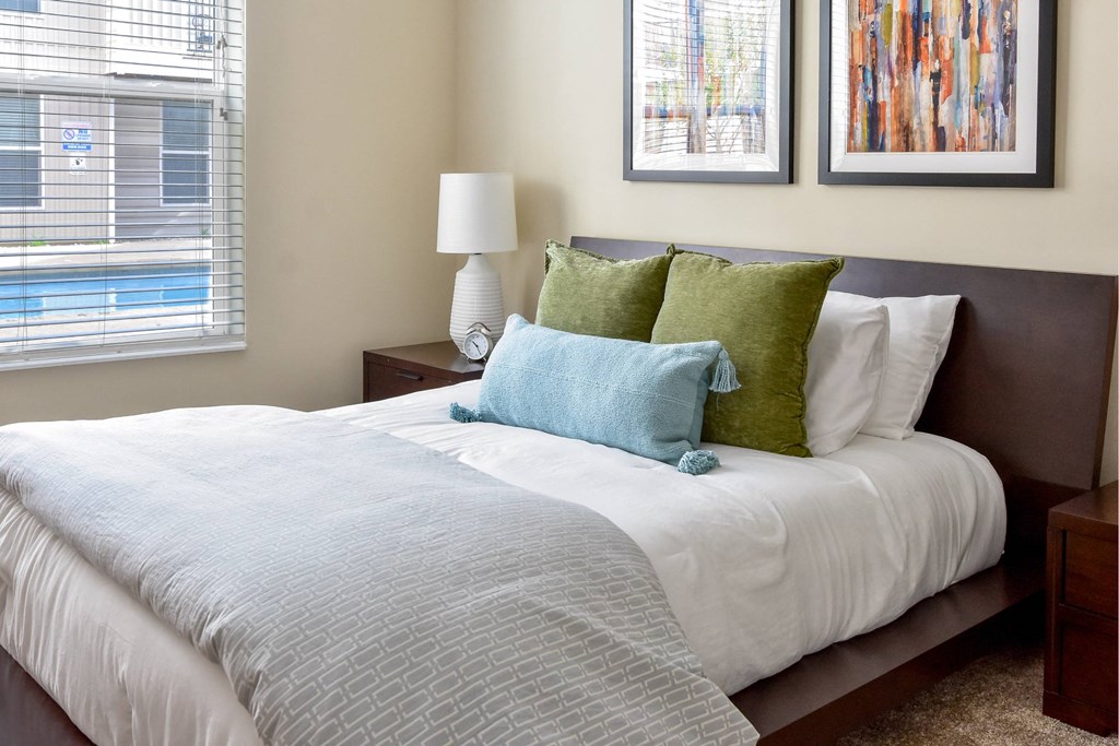 A bed with a white comforter and a blue and green pillow.